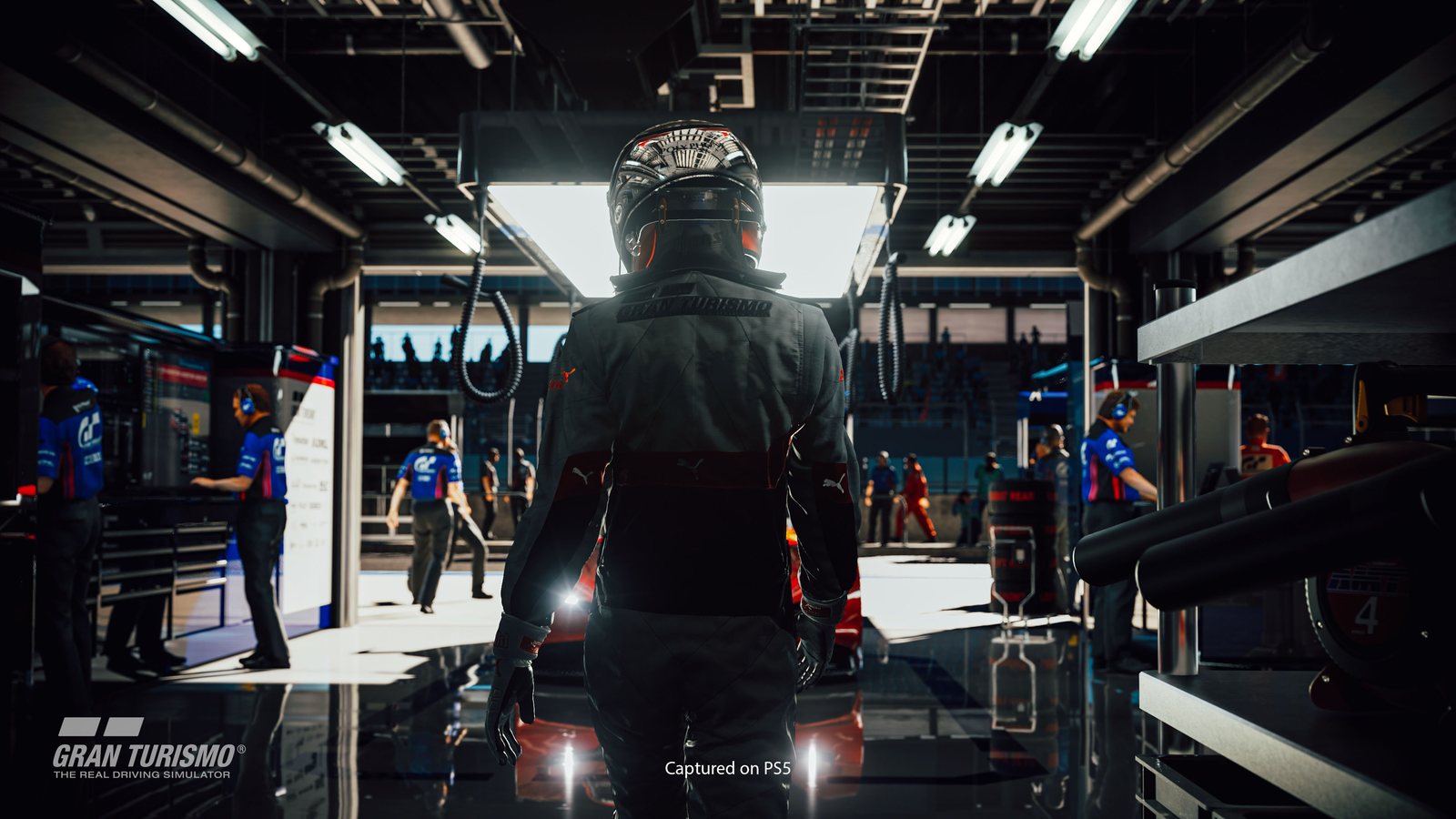 A driver in a helmet walking through the pit garage toward the light